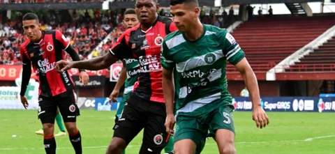 Iván Camacho (verde) busca despejar un balón ante la presión de Yilmar Filigrana (rojinegro) - VizzorImage / Juan Pablo Bayona